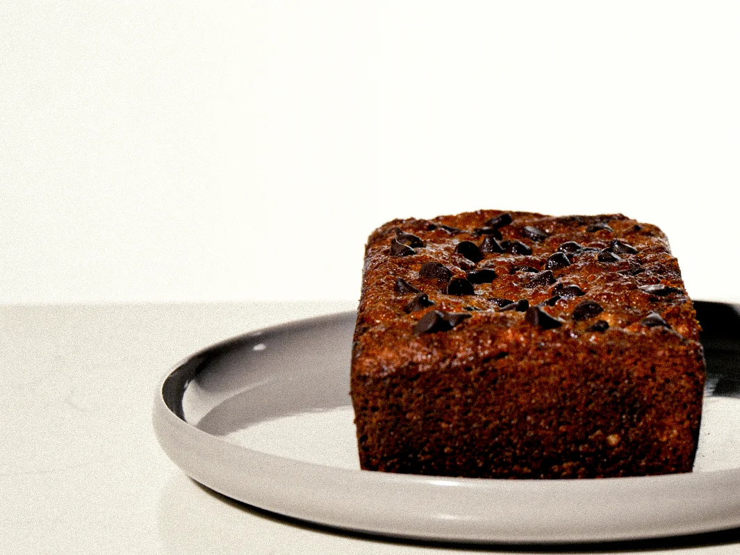 Panqué oscuro con trozos de chocolate sobre un plato gris.
