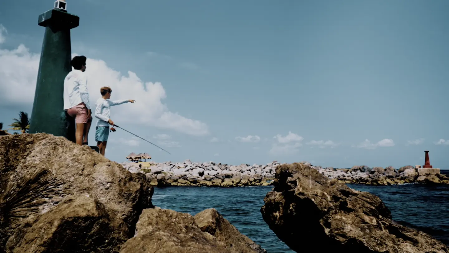 Dos personas pescan entre rocas junto a un faro frente al mar Caribe.