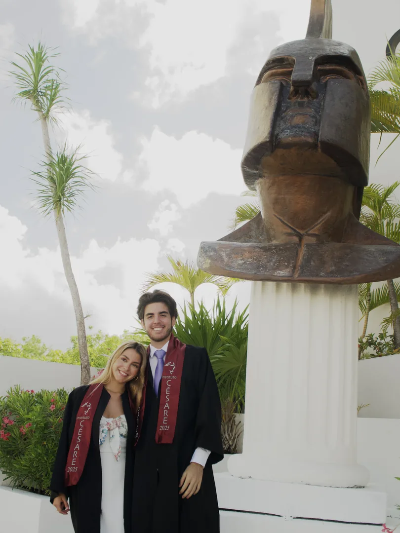 Pareja de graduados abrazados frente a la escultura del casco sobre columnas.