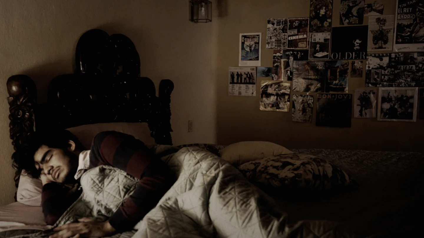Rafael dormido en la cama, pared llena de recortes al fondo.