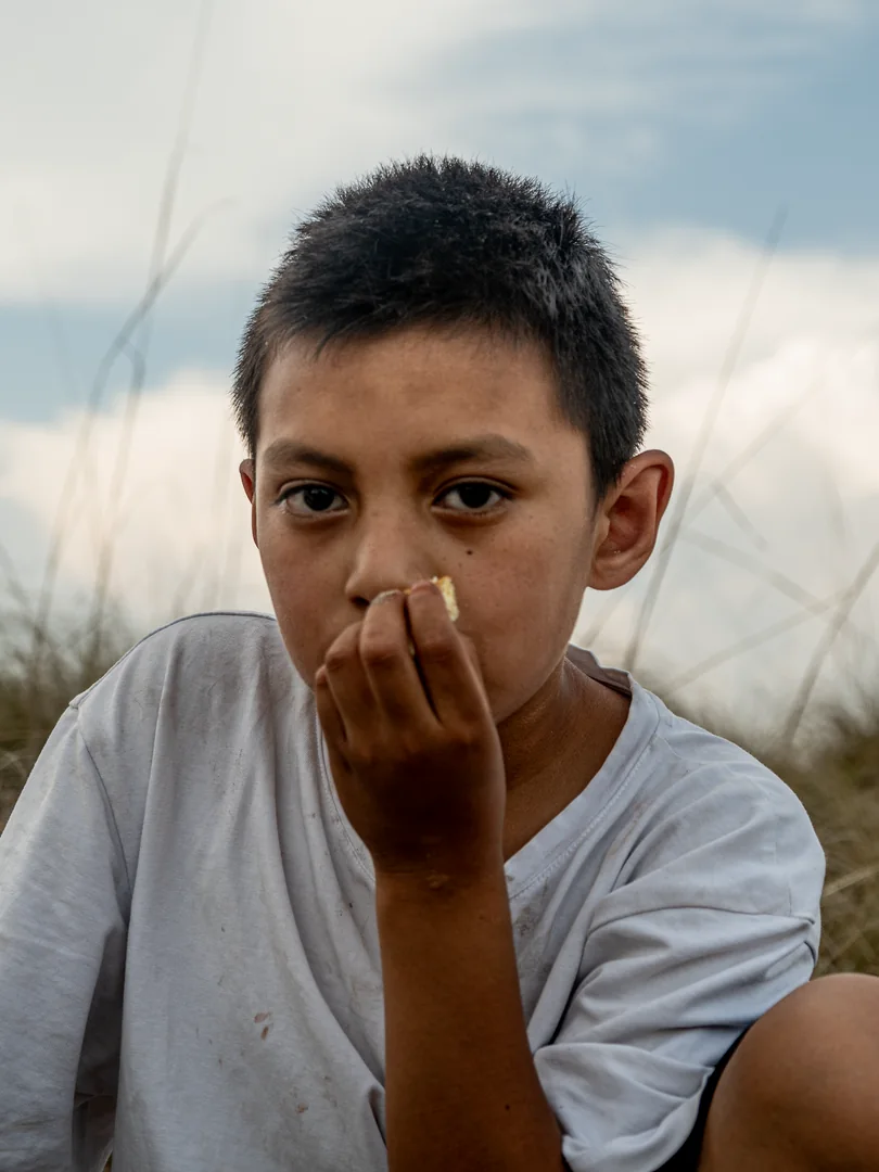 Retrato de un niño con la mano en la boca sentado en el pasto.
