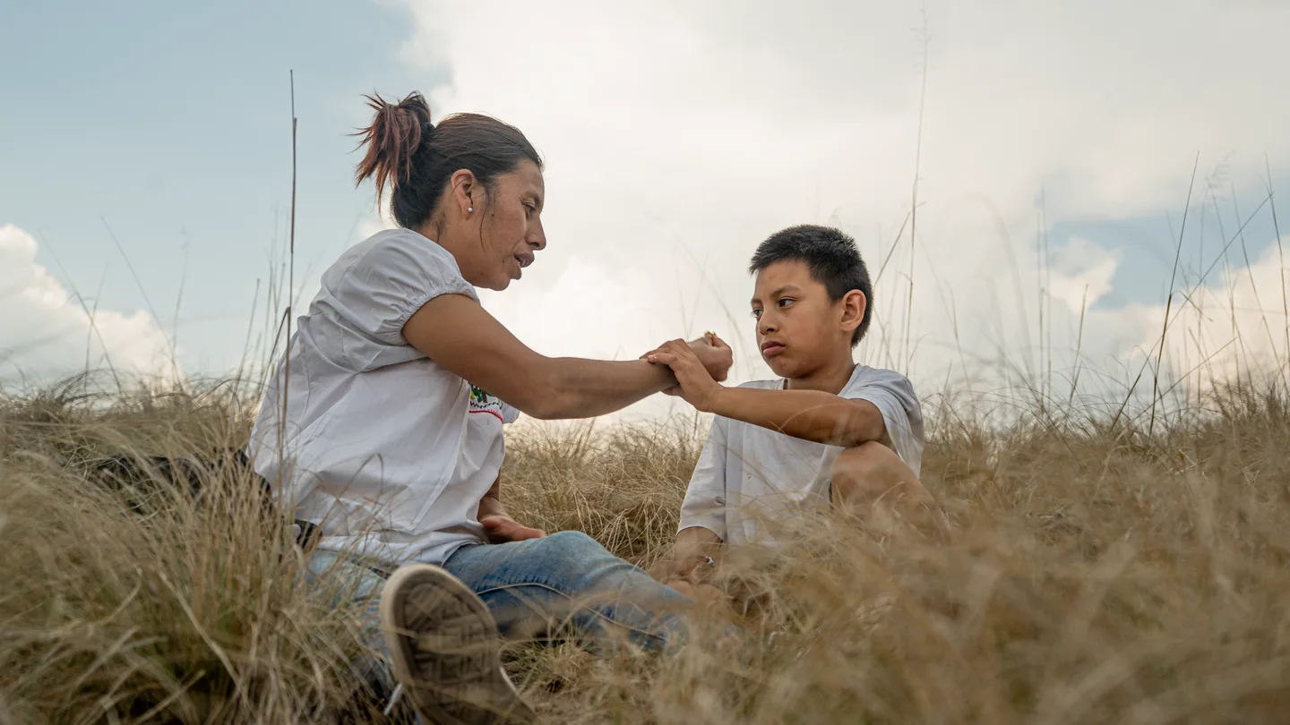 Mujer y niño sentados en el pasto, ella le sostiene el brazo.