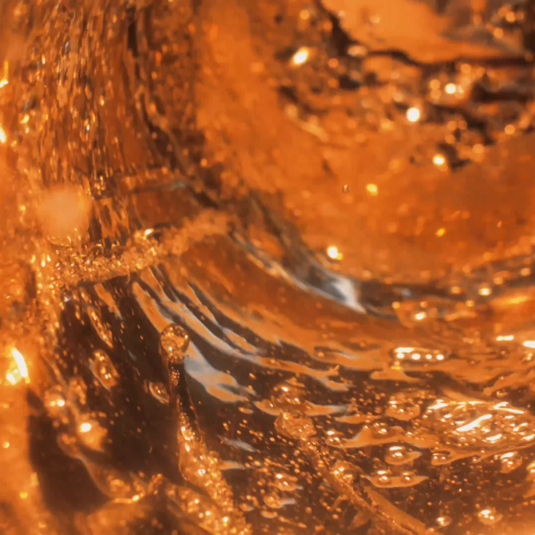 Remolino abstracto de cerveza ámbar con burbujas y reflejos dorados en primer plano.