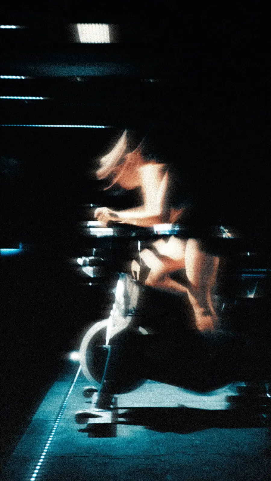 Instructora de spinning pedalea entre reflejos y movimiento dentro del estudio oscuro.