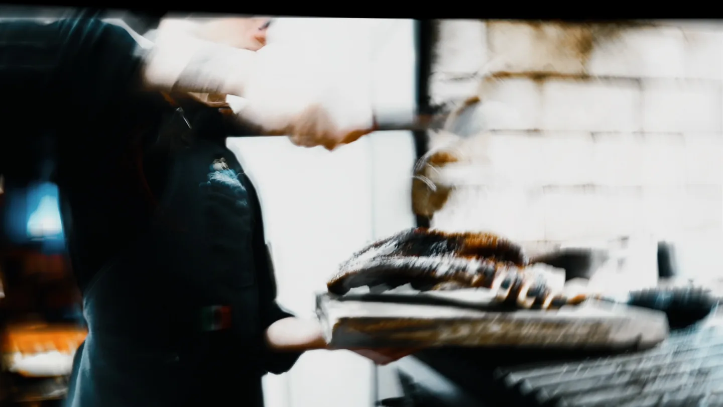 Cocinero con guantes sirve un corte sobre tabla en la cocina.